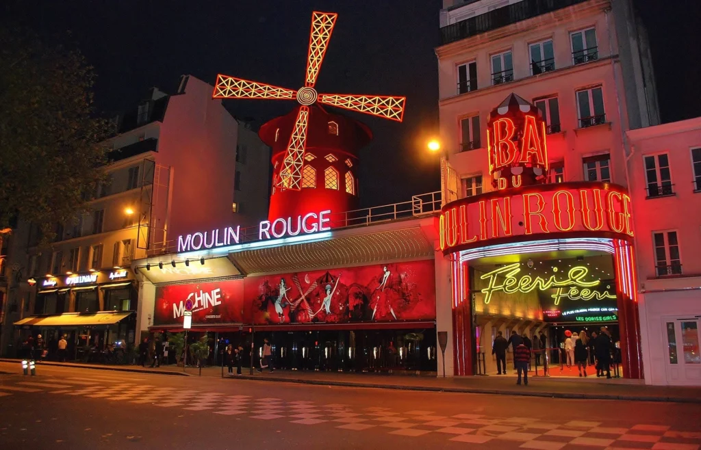 The iconic red windmill of the Moulin Rouge illuminated at night, symbolizing the vibrant energy and allure of this legendary cabaret.
