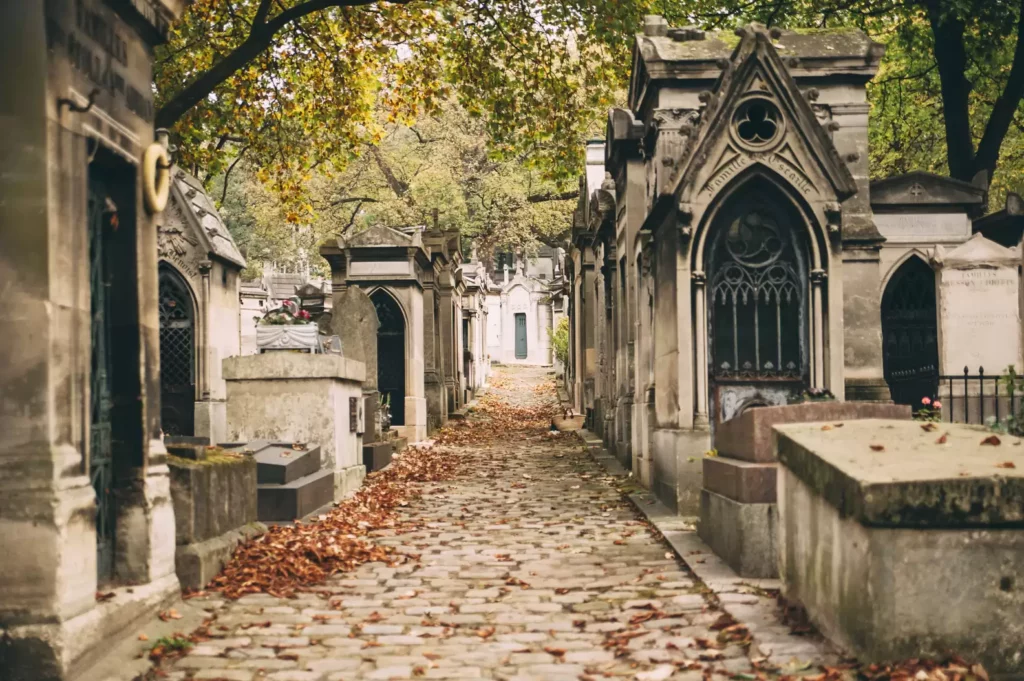 A serene view of Père Lachaise Cemetery, with tombstones and trees lining the pathways.