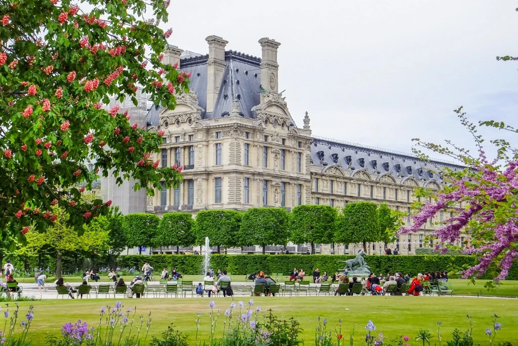 A serene view of the Tuileries Garden in Paris, with beautiful flowers, statues, and the Louvre Museum in the background.